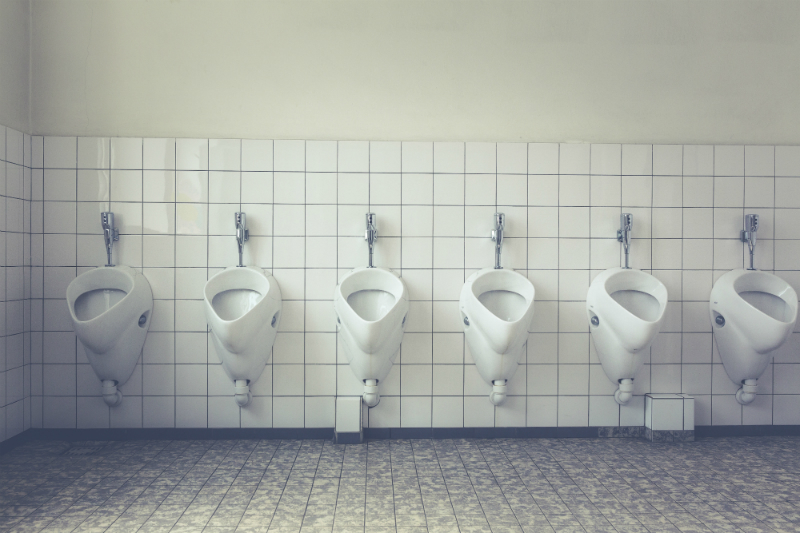 A row of men’s urinals are on display in a partially tiled bathroom.