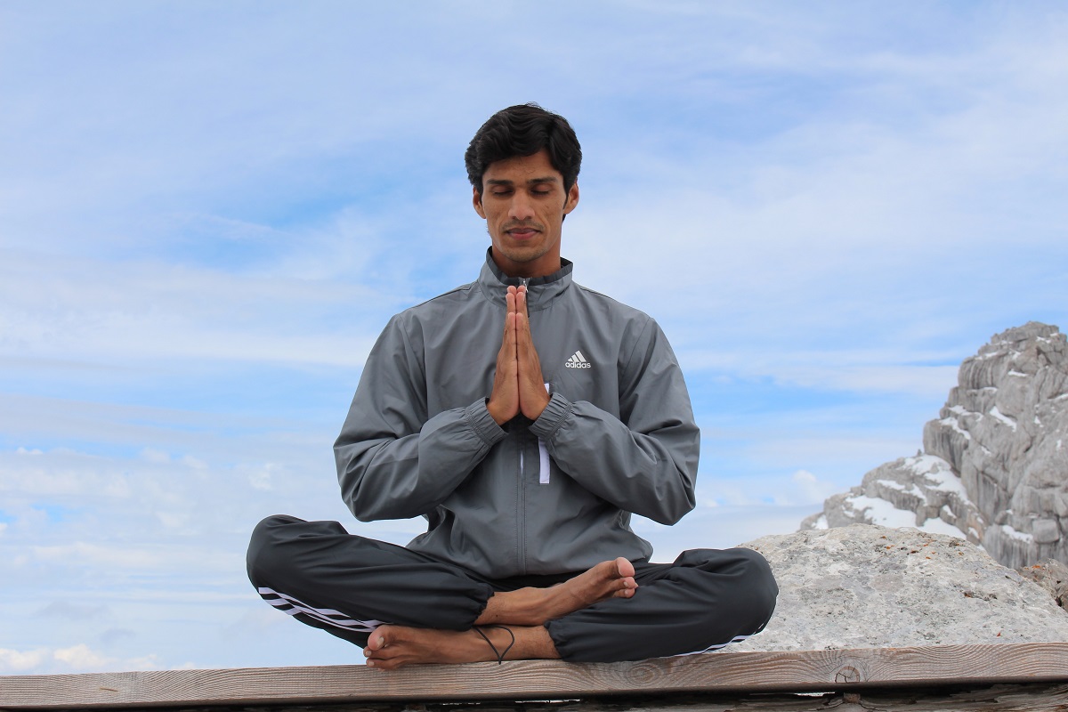Man in grey track suit in seated meditation on mountaintop