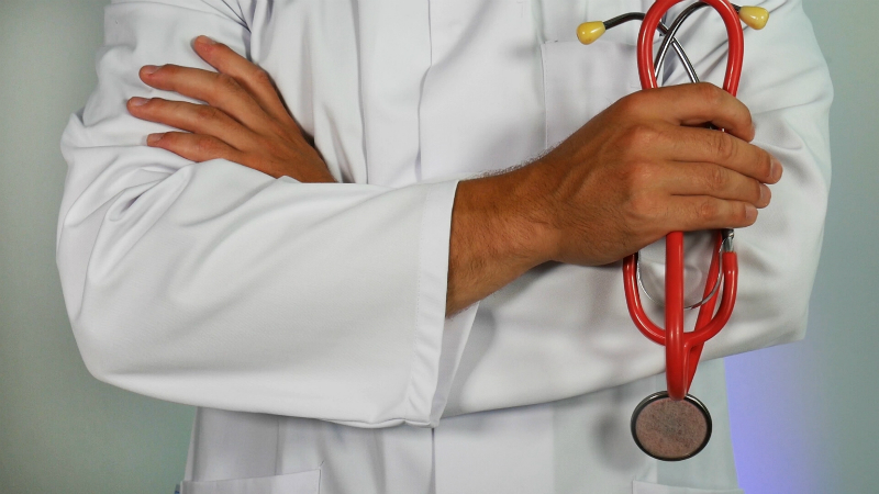 A doctor in a lab coat is crossing their arms and holding a stethoscope.