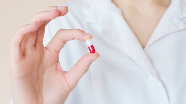 A hand holding up a white and red medication pill