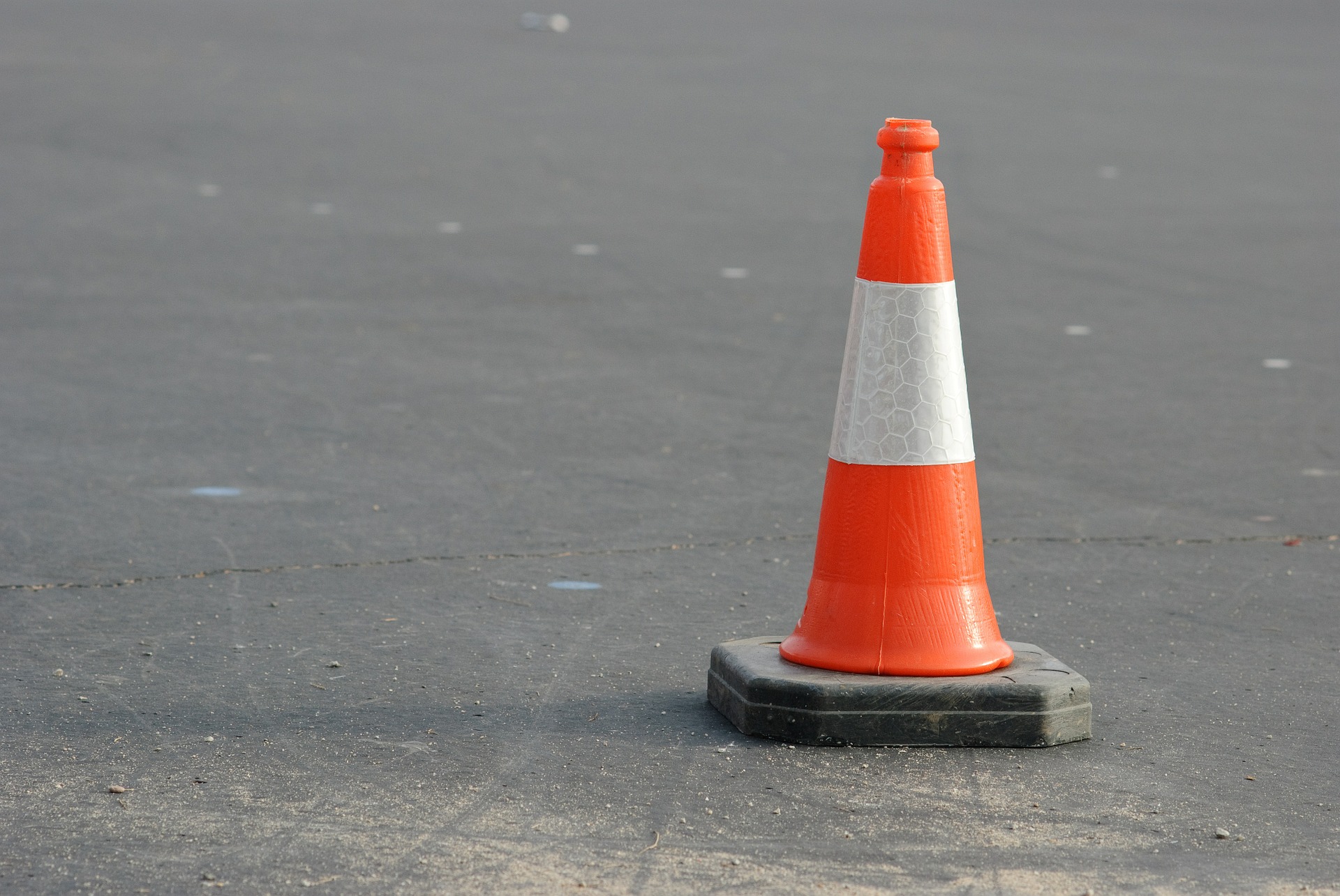 An orange-and-white cone is sitting in the middle of the road.