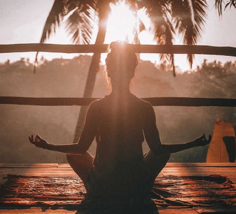 Silhouette of woman in seated yoga pose meditating as sun shines around her