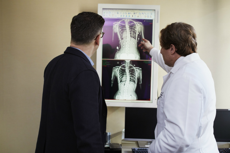 A doctor is pointing at an X-ray next to a patient, explaining what condition the patient has that Cialis can treat.