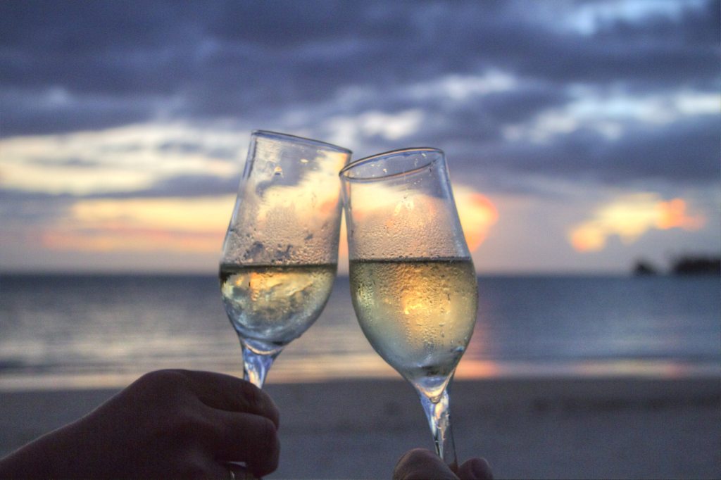 Two clinking glasses of champagne in front of a beach sunset.