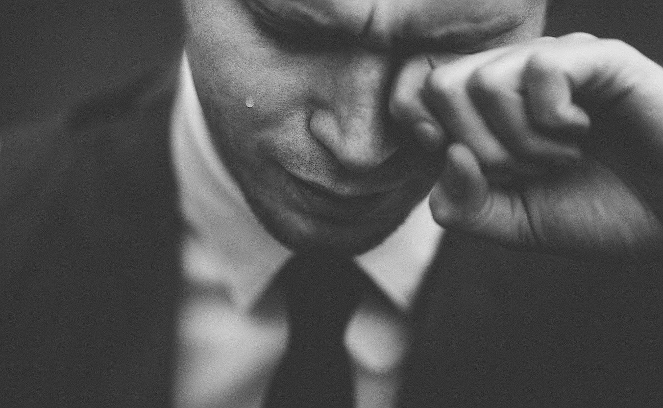 Grayscale image of man in suit wiping tears from eye